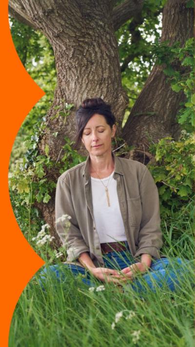 Natalie Fée sat under a tree. She has her eyes closed and is surrounded by long grass.