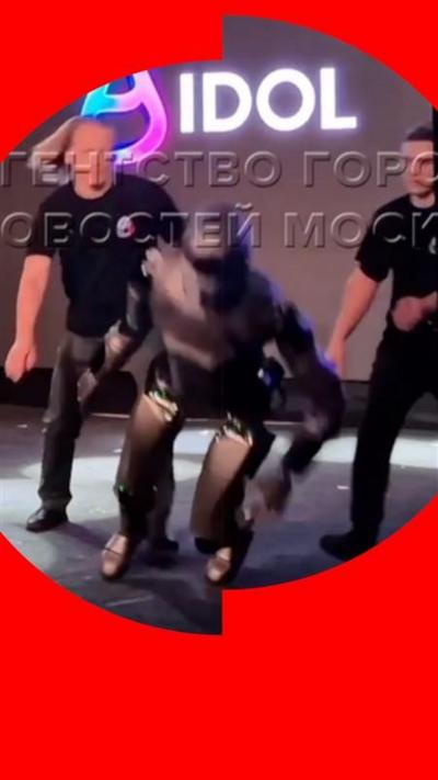 A robot mid-fall, with two men wearing black leaning over to catch it.