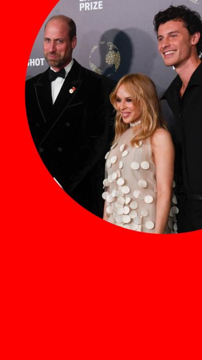 Prince William, in a tuxedo, stands with Kylie Minogue, who wears a nude coloured dress, and Shawn Mendes in a black suit