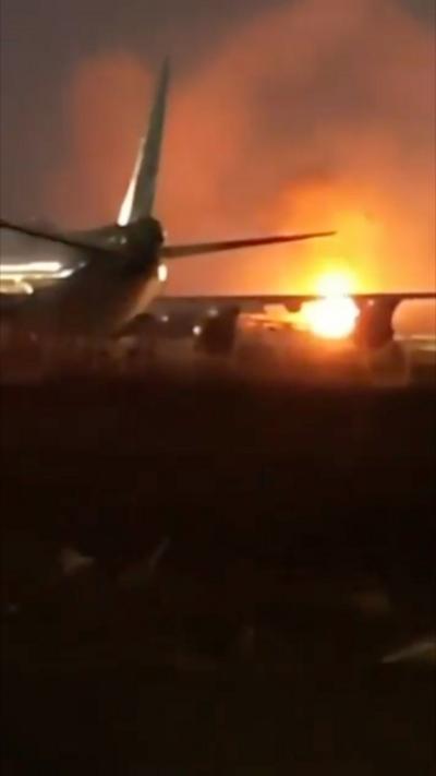 An explosion in the distance, with a plane in the foreground. It is night time. 
