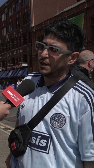 Oasis fan with shades and jersey, being interviewed