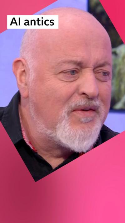 A man, Bill Bailey, Looks confused, he is bald, has a grey beard and is wearing a black shirt