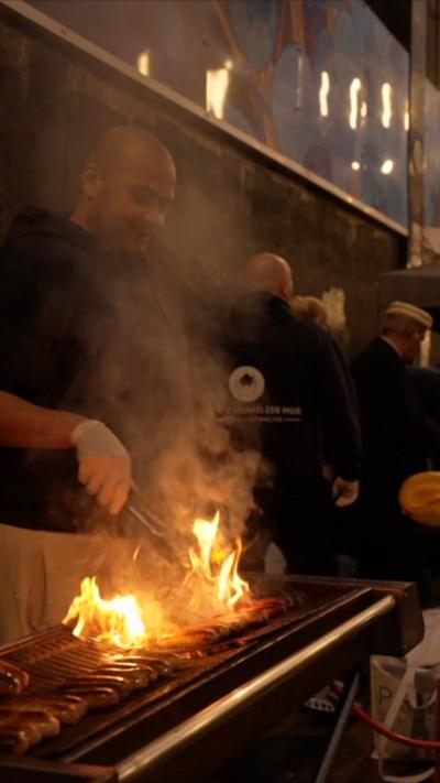 A chef grills sausages over flames, surrounded by smoke.
