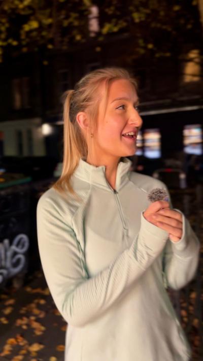 A woman with blonde hair in a white running top in a dark city street.