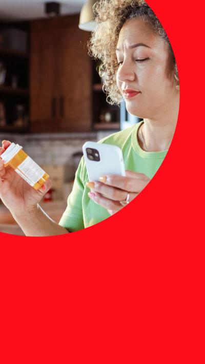 Woman checking prescription bottle while holding her smartphone at home