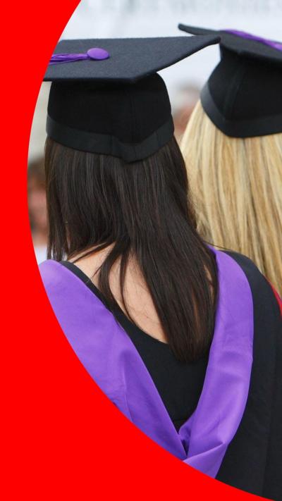 Two women wearing graduation caps and gowns stand with their backs to the camera.