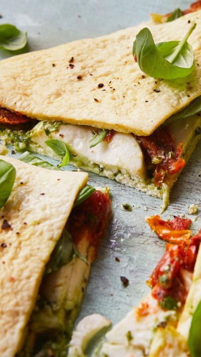 Triangle quarters of a wrap with mozerella, pesto and tomato visible coming inside, scattered with basil.