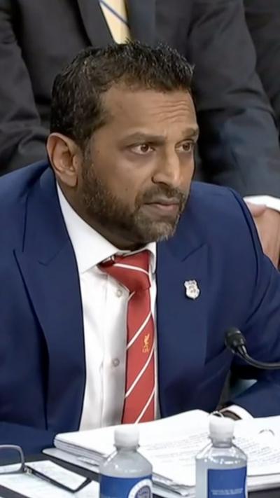 Kash Patel sits behind a table during a US Senate hearing with water bottles and a large binder in front of him.