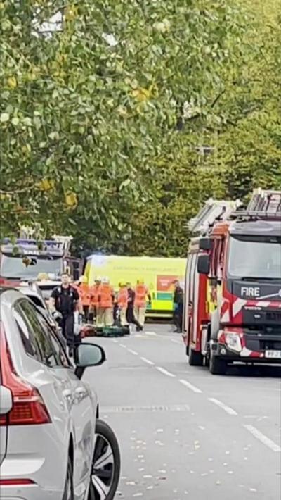 A fire engine, an ambulance and emergency service workers on a tree-lined street