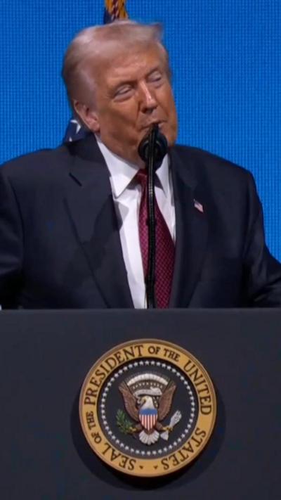 Trump at a lectern with the presidential seal. he is wearing a blue suit and red tie.