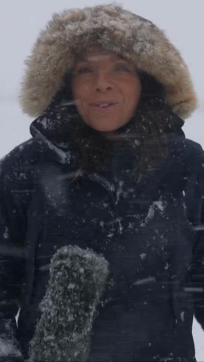 Presenter in a coat with a hood up surrounded by snow falling from the sky