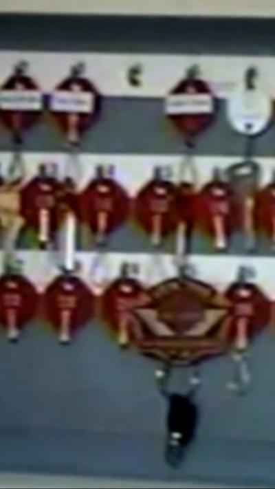 Three rows of red keys, some labelled, hanging from a key rack.