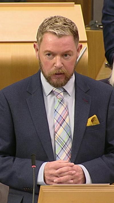 Man with short, grey hair, a dark suit with checked tie and yellow handkerchief.