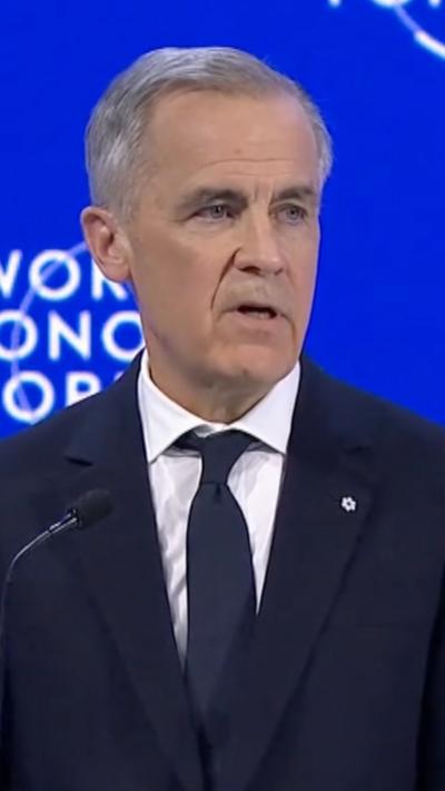 Mark Carney speaks to a mic in front of a blue backgrond.