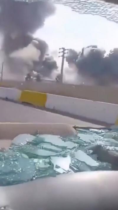 Broken glass in the back of car, shattered window, plume of black smoke in the background