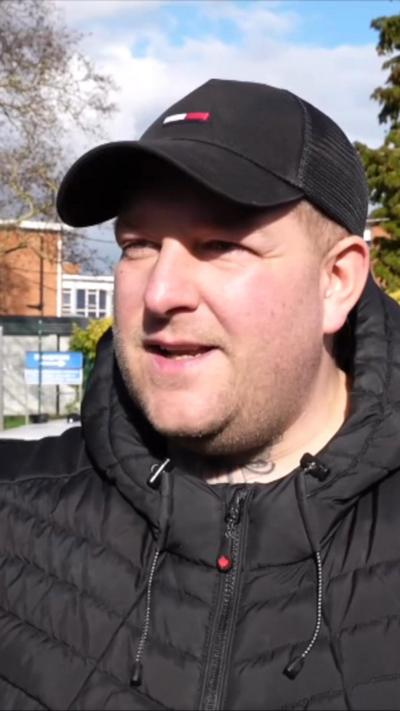 Male parent stands outside school in black coat and black cap