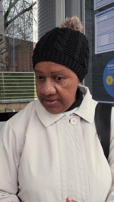 A woman in black bobble hat and white coat at a tram stop