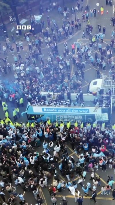 Drone footage of a bus surrounded by hundreds of football fans
