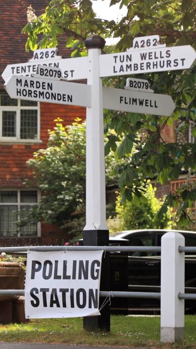 A road sign with a polling station attatched to a fence.