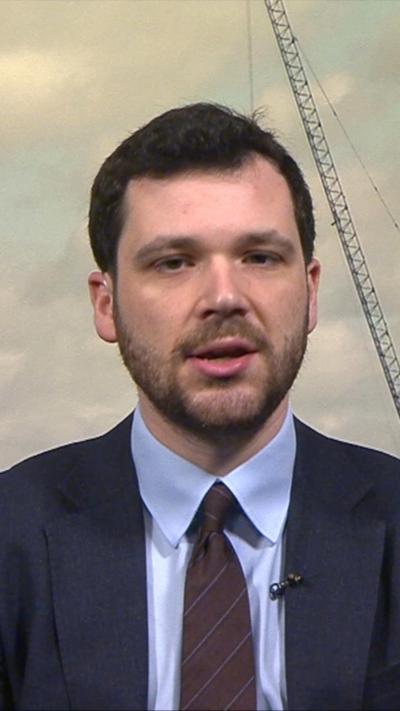 Henry Zefferman wearing a navy blue suit with light blue shirt and maroon tie.