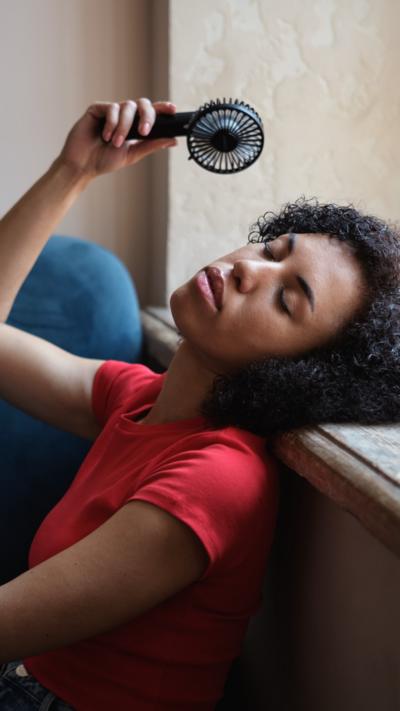Woman in red top sits against a wall with a handheld fan