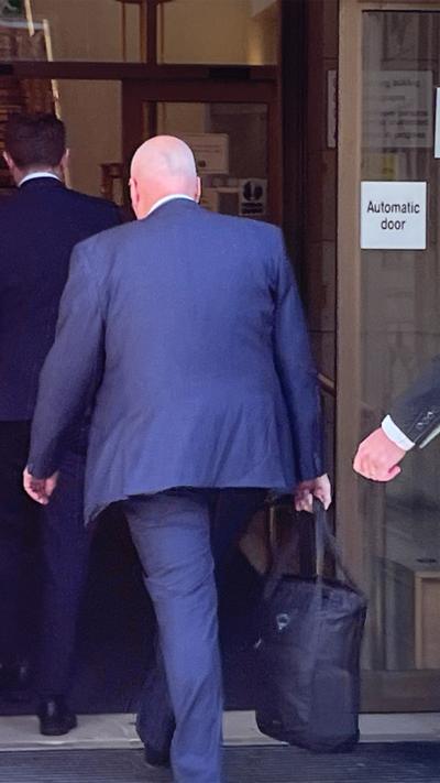 A man in a blue suit enters into a building holding an overnight bag.