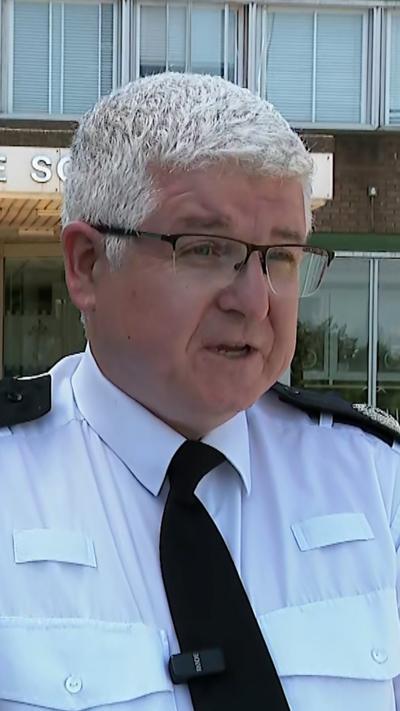 A head and shoulders shot of a police officer in a white shirt and glasses. He has a small mic clipped onto his tie.