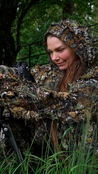 Hannah Stitfall looks at the back of her camera while in camo gear in a field