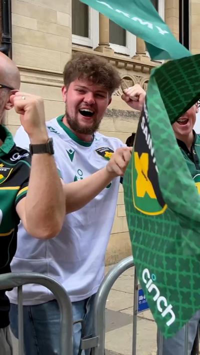 A smiling man waves a Saints banner while dressed in a Saints shirt.