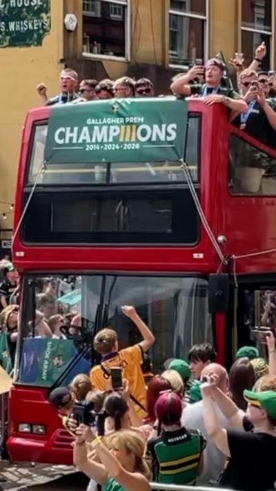 A large red double decker bus surrounded by crowds with people dressed in Saints kits on the open roof