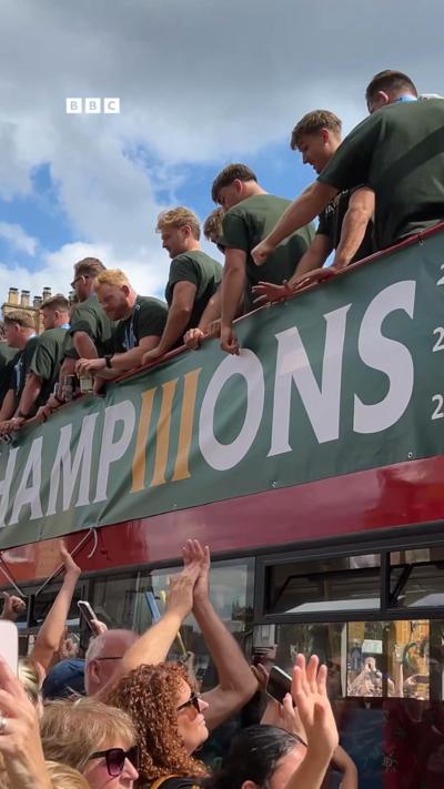 An open top bus with rugby players drivers past cheering crowds