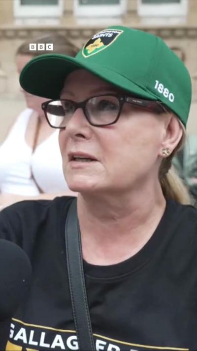 A woman is speaking to a microphone while wearing a Saints cap