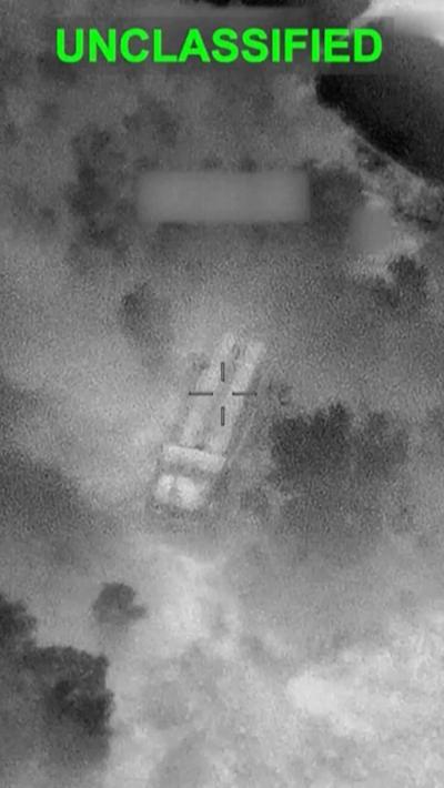 Blurry black and white image with a crosshair on a target near what could be smoke