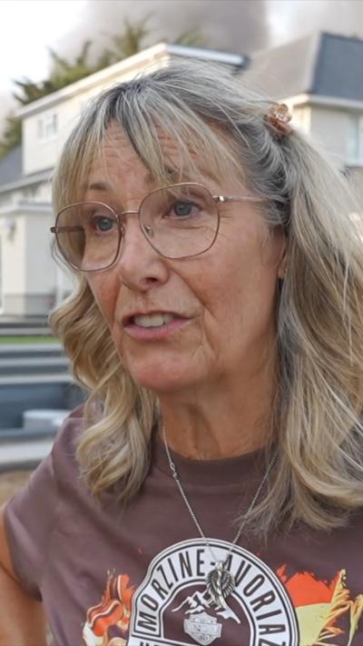 Woman with shoulder length greying blond hair wearing glasses and wearing a brown t-shirt