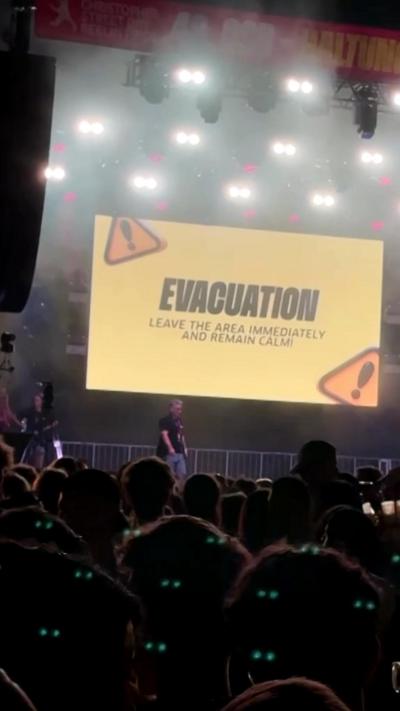 A yellow sign on a stage reads "evacuation" in front of crowd.