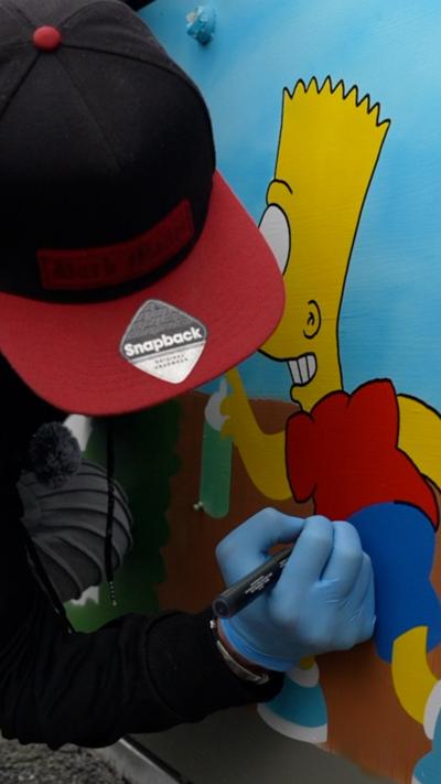 A person wearing a black and red cap uses a marker to draw on a colourful mural