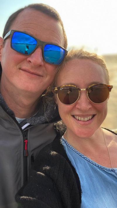 Husband and wife on beach smiling wearing sunglasses