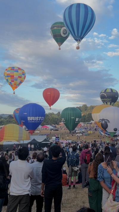 Hot air balloons with a blue sky background and people watching taking photos.