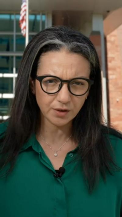 A woman in glasses and a green shirt standing outside the courthouse. The American flag is in the background.