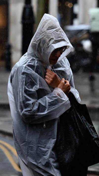 Person in a mac walks along street in the rain