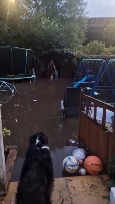 A garden is flooded with water with a trampoline and shed at the bottom of the garden.
