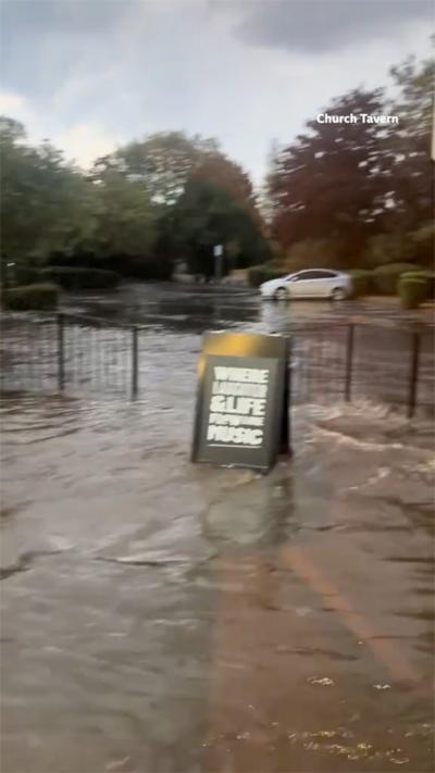 A beer garden is flooded in water with a sign advertising for drinks