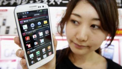 An employee of Japan's largest mobile carrier NTT Docomo Inc holds a Samsung Galaxy S III smartphone