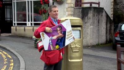 A postman holds an 'Andy Murray stamp' beside the gold post box in Dunblane