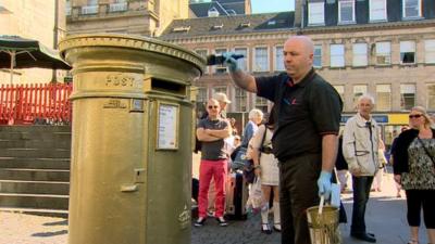 A man paints a post box gold for Sir Chris Hoy's second Olympic gold medal win