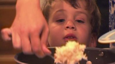 Boy looking intensely as food is served by mum from a pot.