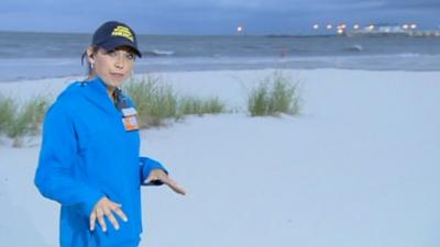 Meteorologist Ginger Zee on the beach in front of growing surf in Gulfport, Mississippi