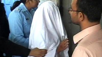 Rimsha with a blanket over her head being escorted by a policewoman