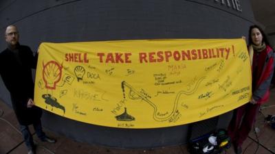 Friends of the Earth campaigners holding a banner demanding Shell take responsibility for the leaks in Nigeria