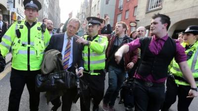 UKIP leader Nigel Farage being escorted by police officers as he leaves the Cannons Gait pub as protestors heckle him